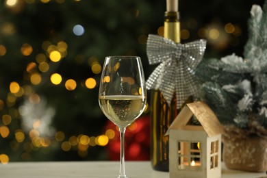 Glass of white wine and Christmas decor on table against blurred lights, space for text. Bokeh effect