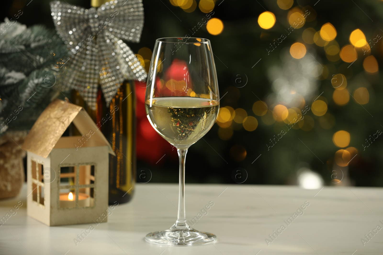 Photo of Glass of white wine and Christmas decor on table against blurred lights, space for text. Bokeh effect