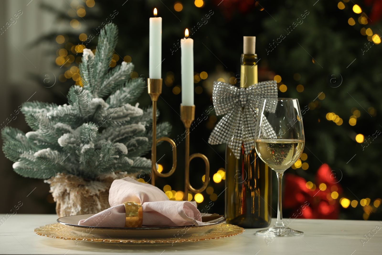 Photo of White wine, plates, burning candles and decor on table against blurred Christmas lights. Bokeh effect