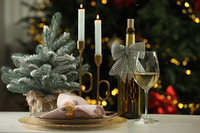 White wine, plates, burning candles and decor on table against blurred Christmas lights. Bokeh effect