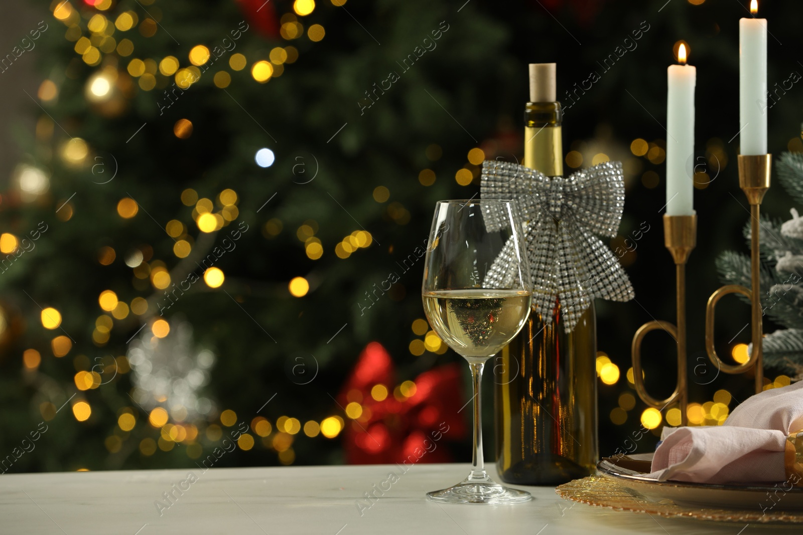 Photo of White wine, plates, burning candles and decor on table against blurred Christmas lights, space for text. Bokeh effect