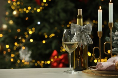 Photo of White wine, plates, burning candles and decor on table against blurred Christmas lights, space for text. Bokeh effect