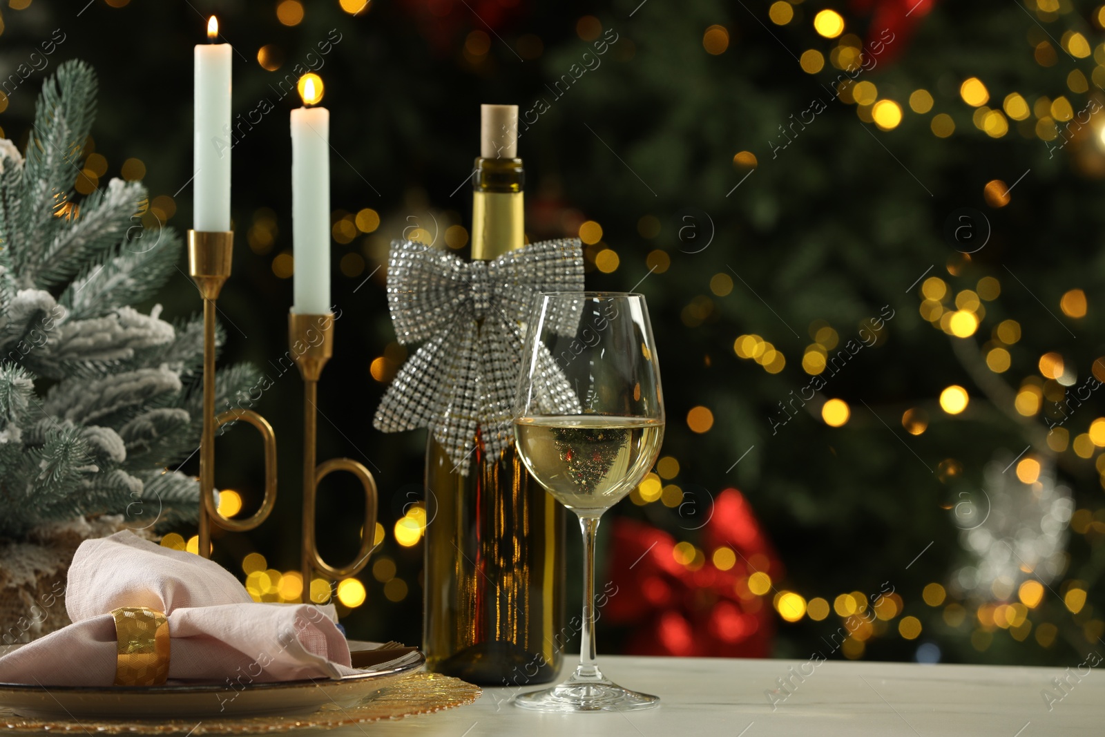 Photo of White wine, plates, burning candles and decor on table against blurred Christmas lights. Bokeh effect