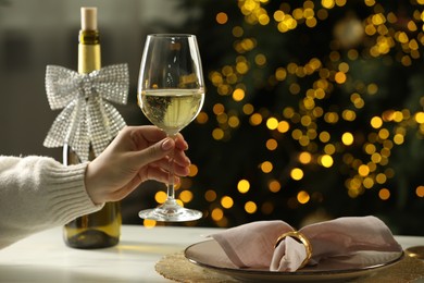 Woman with glass of white wine at table against blurred Christmas lights, closeup and space for text. Bokeh effect