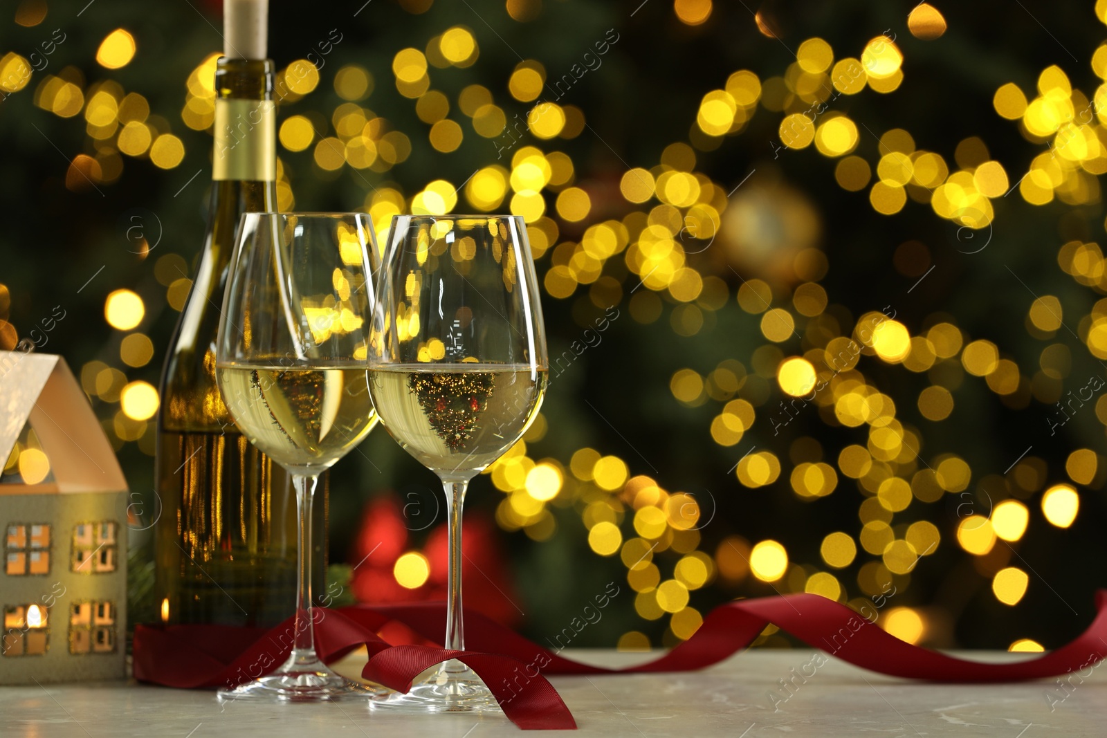 Photo of Glasses of white wine and Christmas decor on table against blurred lights, space for text. Bokeh effect