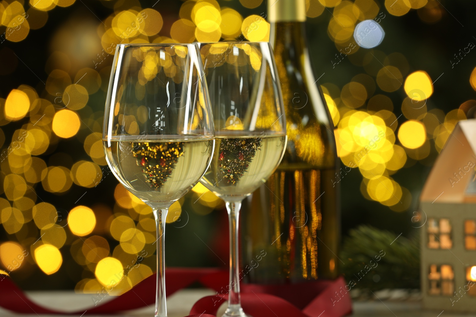 Photo of Glasses of white wine and Christmas decor on table against blurred lights, closeup. Bokeh effect