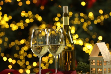 Photo of Glasses of white wine and Christmas decor on table against blurred lights. Bokeh effect