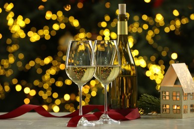 Photo of Glasses of white wine and Christmas decor on table against blurred lights. Bokeh effect