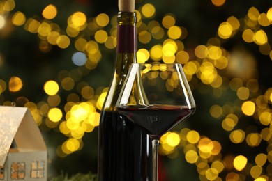 Photo of Bottle and glass of red wine against blurred Christmas lights, closeup. Bokeh effect