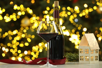 Photo of Glass of red wine and Christmas decor on table against blurred lights. Bokeh effect