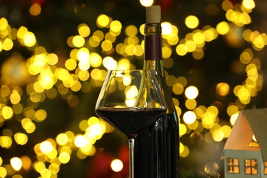 Photo of Bottle and glass of red wine against blurred Christmas lights, closeup. Bokeh effect