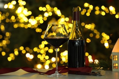 Photo of Glass of red wine and Christmas decor on table against blurred lights. Bokeh effect