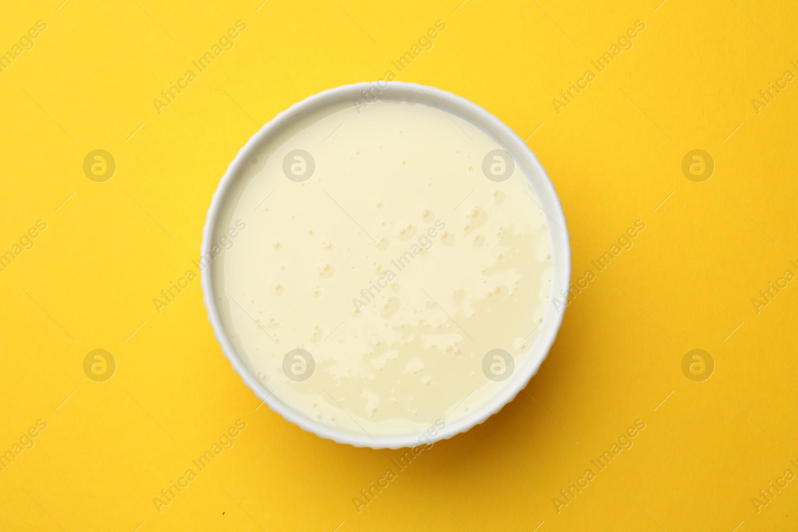 Photo of Tasty condensed milk in bowl on orange background, top view