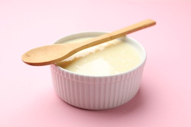 Photo of Tasty condensed milk in bowl and spoon on light pink background, closeup