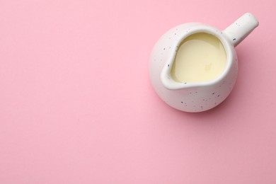 Photo of Tasty condensed milk in jug on light pink background, top view. Space for text