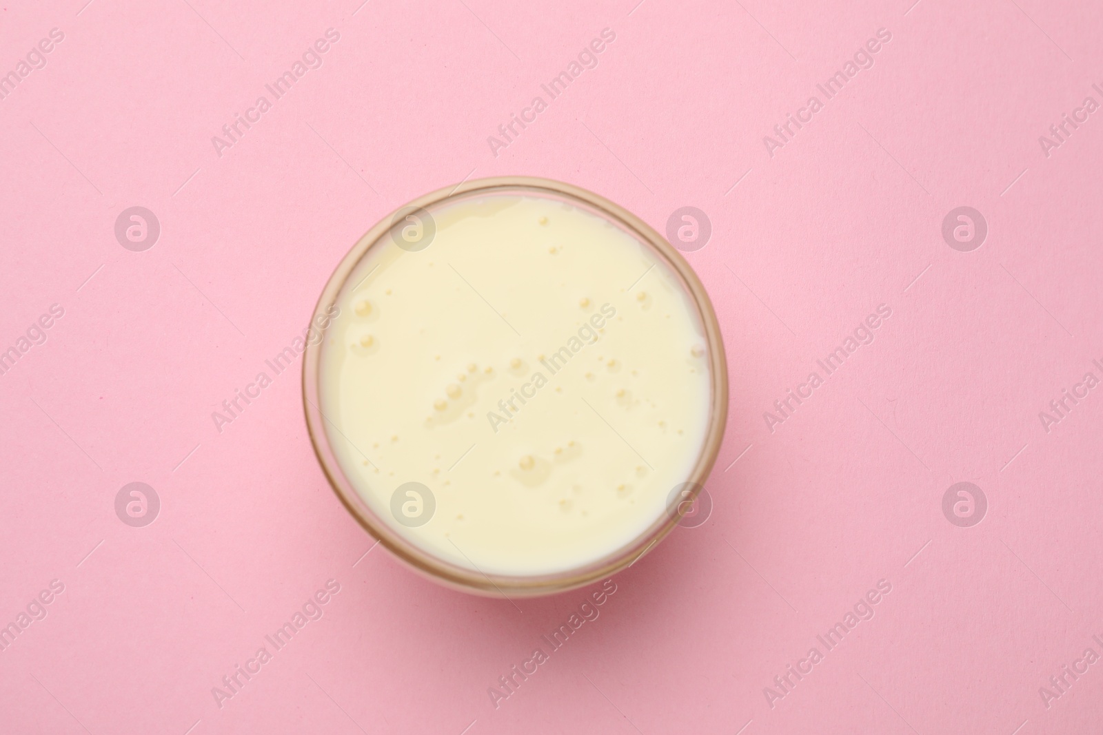 Photo of Tasty condensed milk in bowl on light pink background, top view