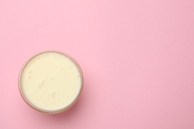 Photo of Tasty condensed milk in bowl on light pink background, top view. Space for text