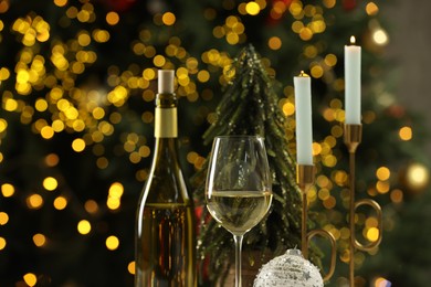 Photo of Bottle and glass of white wine with Christmas decor against blurred lights, closeup. Bokeh effect