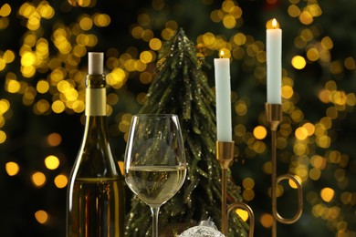 Photo of Bottle and glass of white wine with Christmas decor against blurred lights, closeup. Bokeh effect