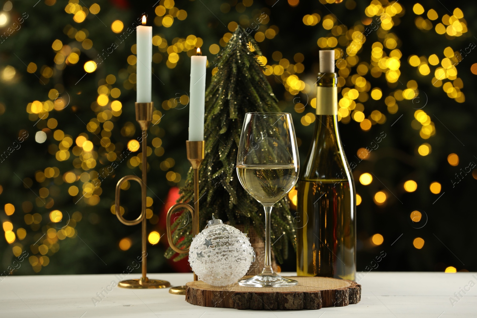 Photo of Glass and bottle of white wine with Christmas decor on table against blurred lights. Bokeh effect