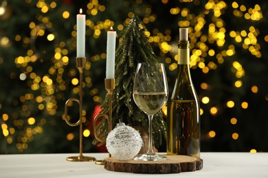 Photo of Glass and bottle of white wine with Christmas decor on table against blurred lights. Bokeh effect