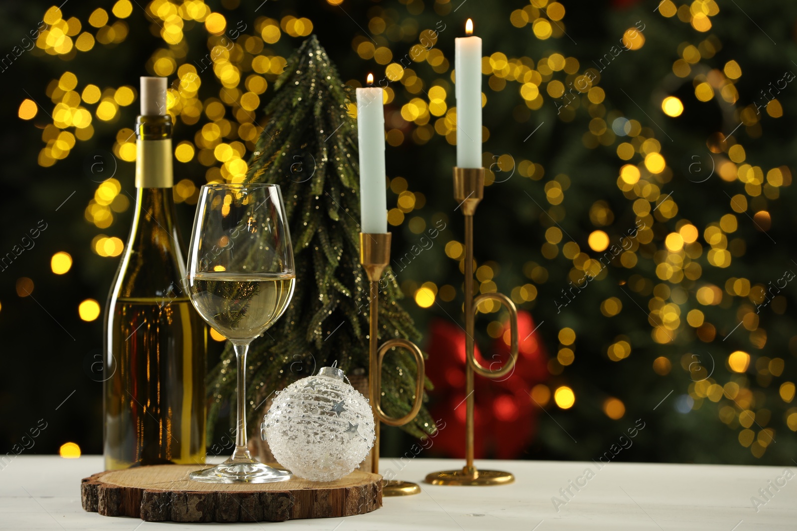 Photo of Glass and bottle of white wine with Christmas decor on table against blurred lights. Bokeh effect