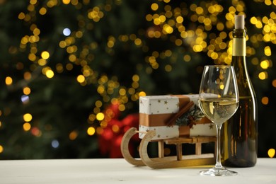 Photo of Glass and bottle of white wine with Christmas decor on table against blurred lights, space for text. Bokeh effect