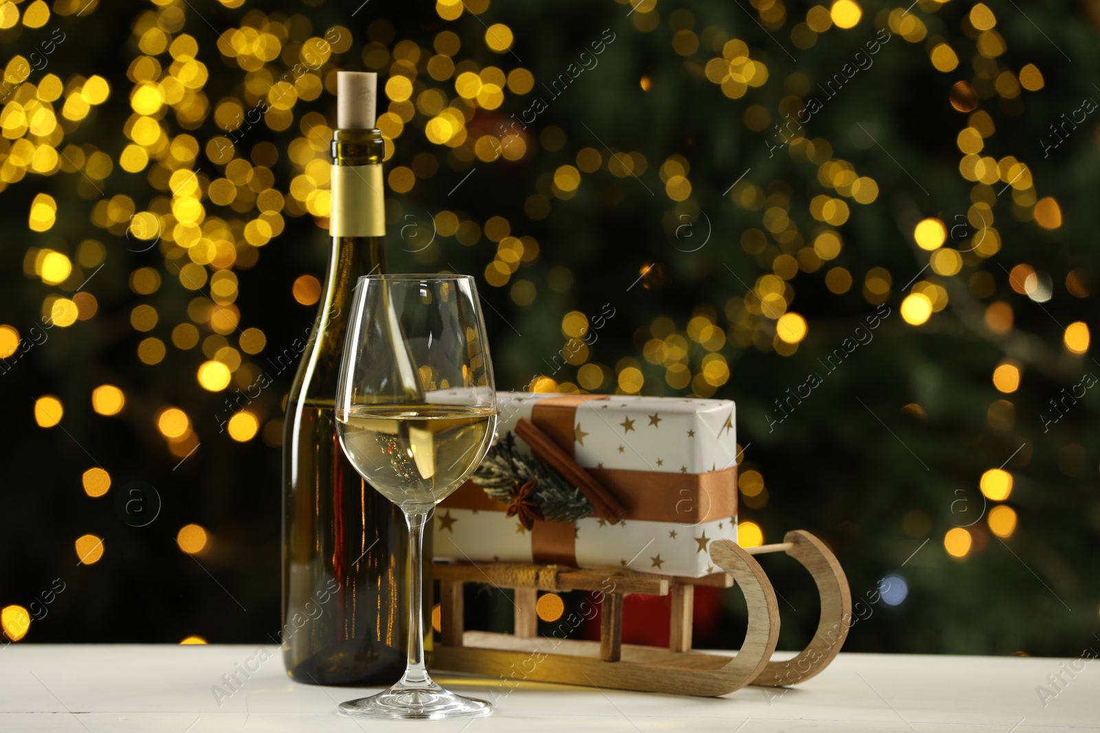 Photo of Glass and bottle of white wine with Christmas decor on table against blurred lights. Bokeh effect