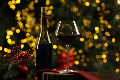 Photo of Glass and bottle of red wine with Christmas decor on wooden table against blurred lights. Bokeh effect