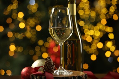 Photo of Glass and bottle of white wine with Christmas decor on table against blurred lights, closeup. Bokeh effect