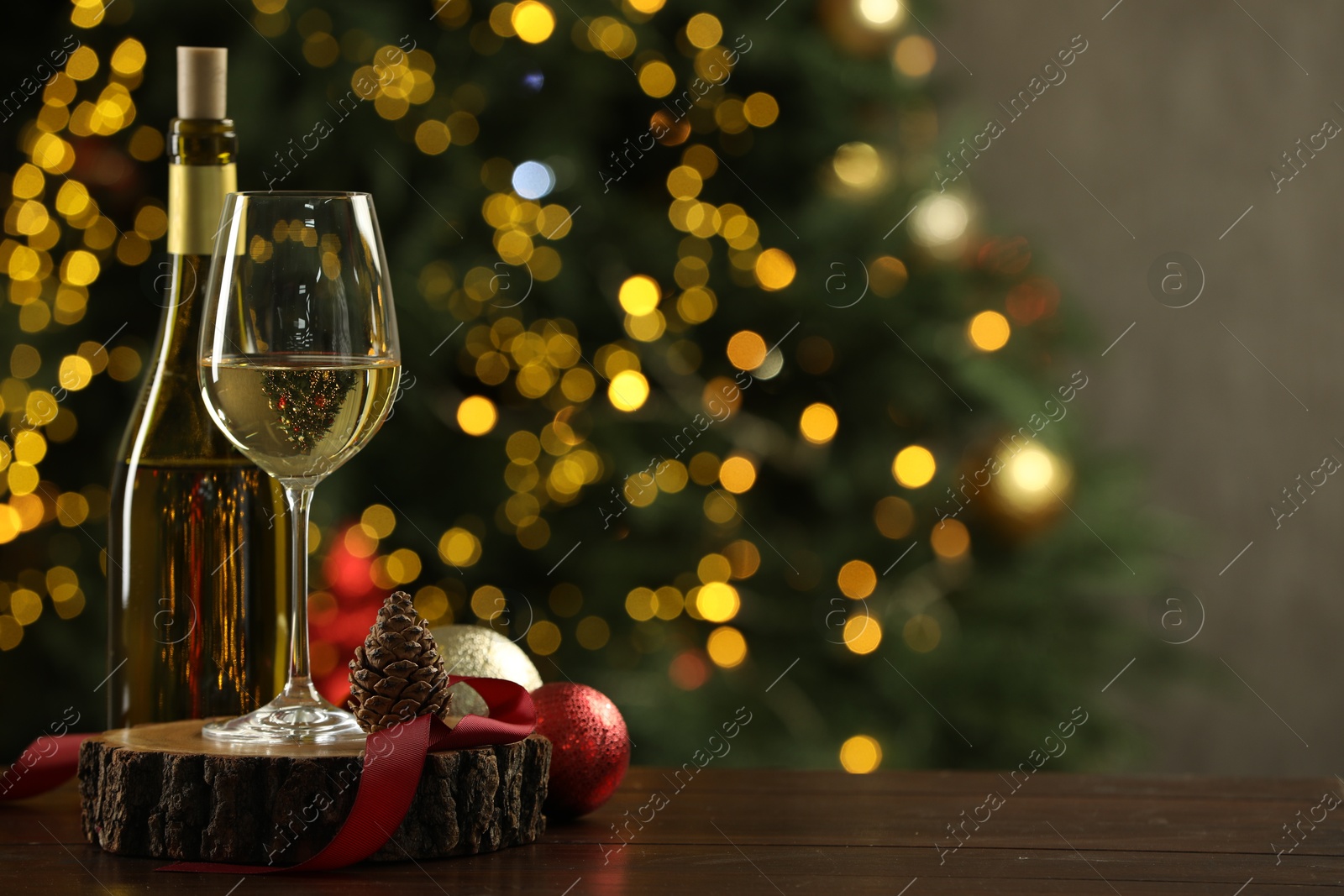 Photo of Glass and bottle of white wine with Christmas decor on wooden table against blurred lights, space for text. Bokeh effect