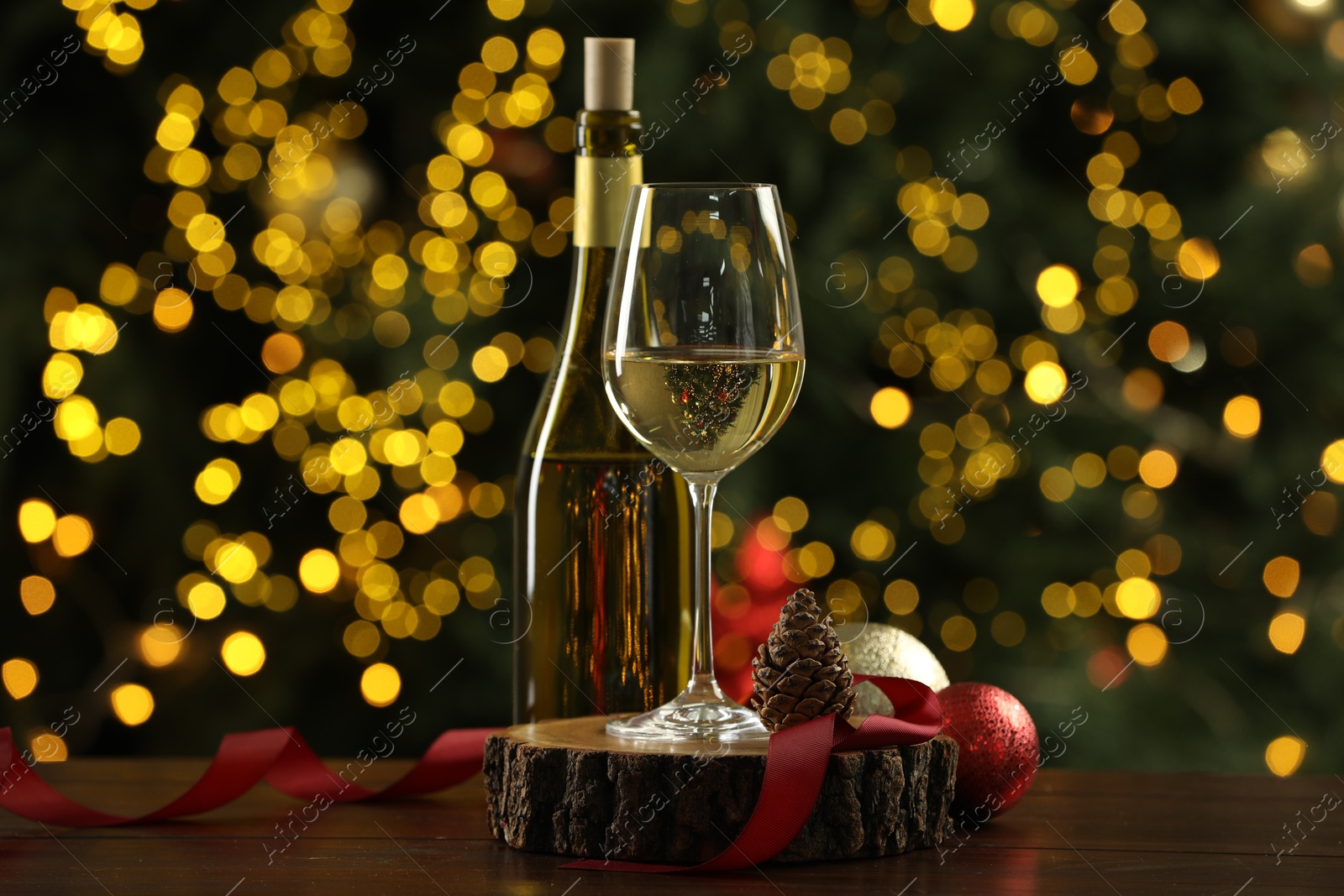 Photo of Glass and bottle of white wine with Christmas decor on wooden table against blurred lights. Bokeh effect