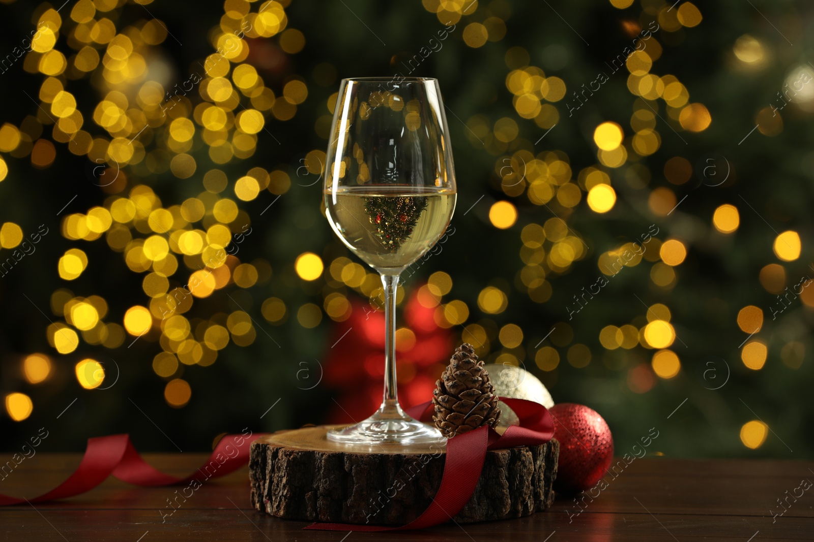 Photo of Glass of white wine with Christmas decor on wooden table against blurred lights. Bokeh effect