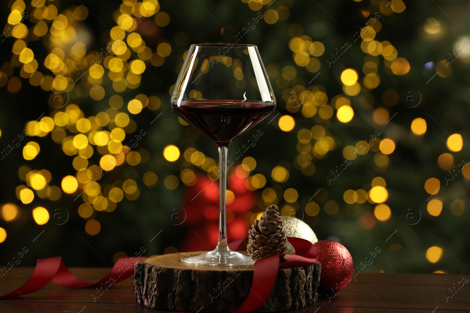 Photo of Glass of red wine with Christmas decor on wooden table against blurred lights. Bokeh effect