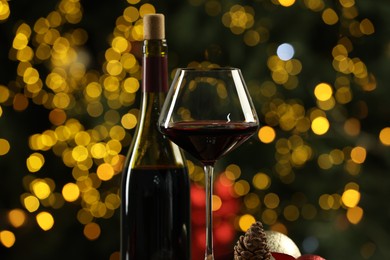 Bottle and glass of red wine against blurred Christmas lights, closeup. Bokeh effect