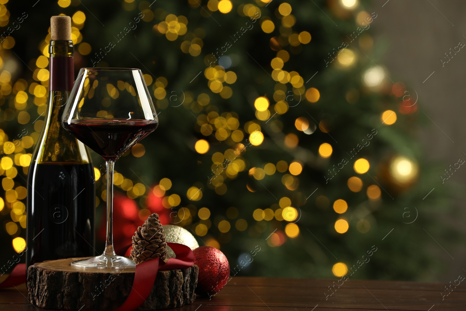 Photo of Glass and bottle of red wine with Christmas decor on wooden table against blurred lights, space for text. Bokeh effect