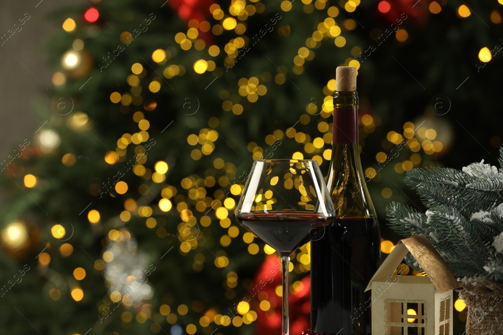 Photo of Bottle and glass of red wine with Christmas decor against blurred lights, space for text. Bokeh effect