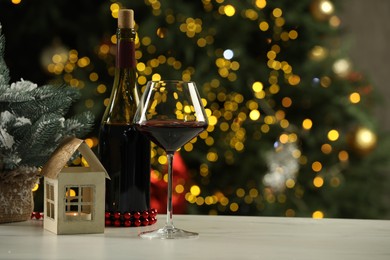 Photo of Glass and bottle of red wine with Christmas decor on table against blurred lights, space for text. Bokeh effect