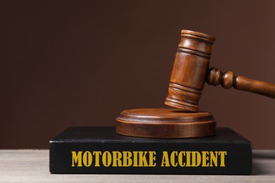 Image of Motorbike Accident law book and judge's gavel on wooden table against brown background, space for text