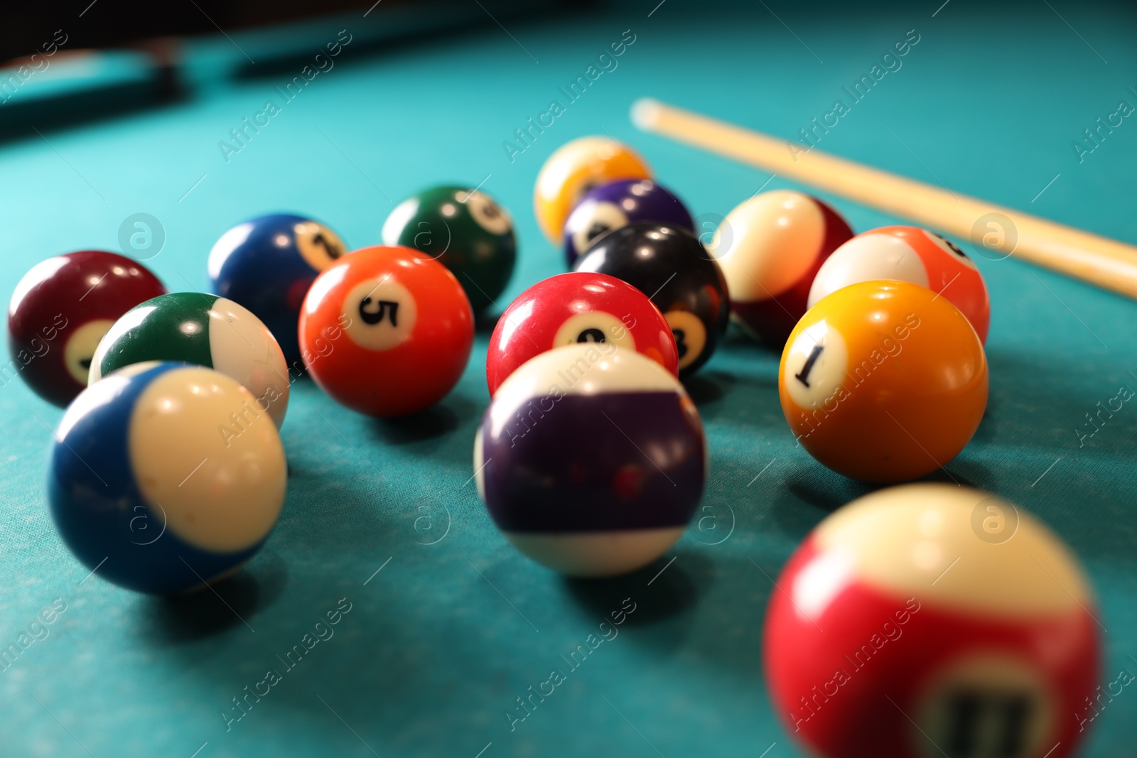 Photo of Many colorful billiard balls and cue on green table, closeup