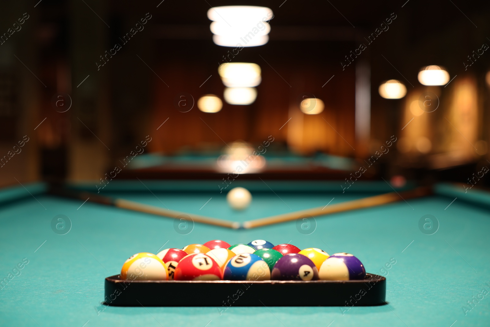 Photo of Plastic triangle rack with billiard balls and cues on green table indoors