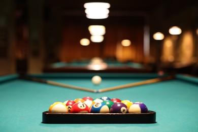 Photo of Plastic triangle rack with billiard balls and cues on green table indoors