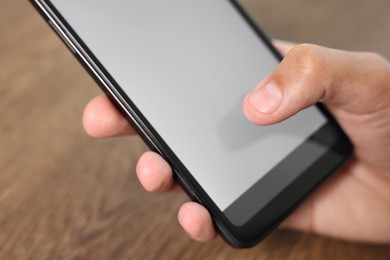 Photo of Man unlocking smartphone with fingerprint scanner at wooden table, closeup