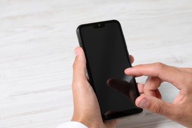 Photo of Man unlocking smartphone with fingerprint scanner at light wooden table, closeup