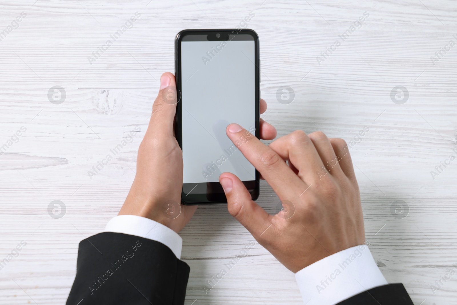 Photo of Man unlocking smartphone with fingerprint scanner at light wooden table, top view