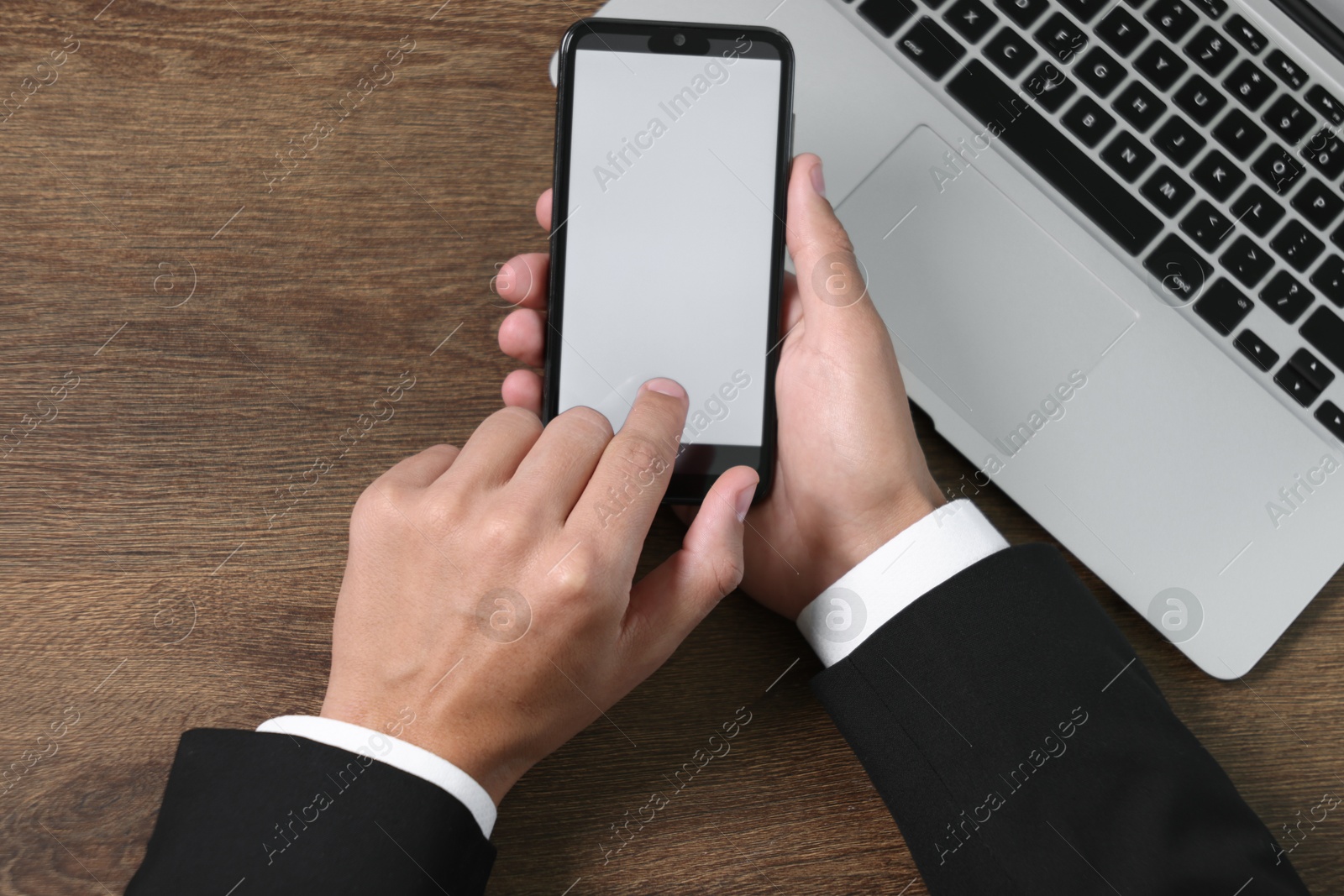 Photo of Man unlocking smartphone with fingerprint scanner near laptop at wooden table, top view