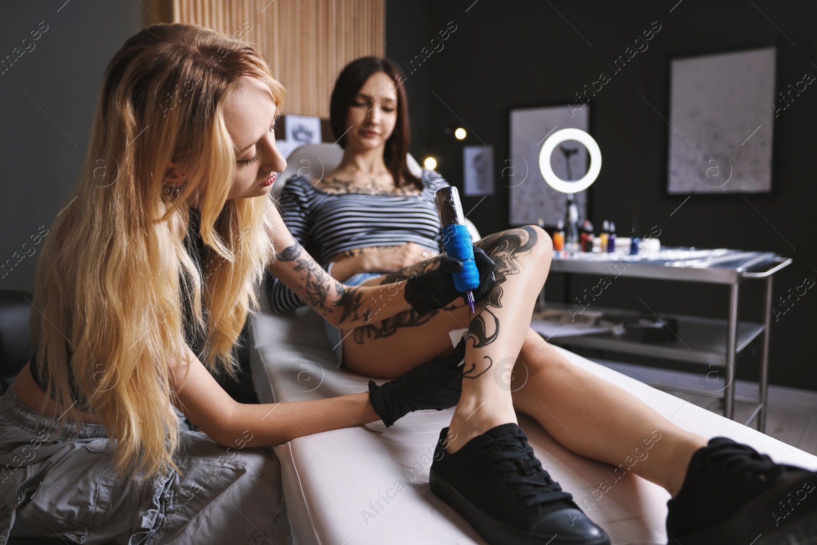 Photo of Professional artist tattooing woman's leg with machine in salon