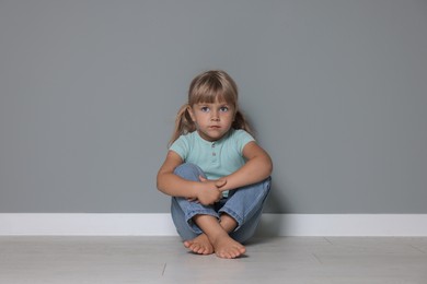 Orphanage concept. Sad little girl sitting on floor near grey wall