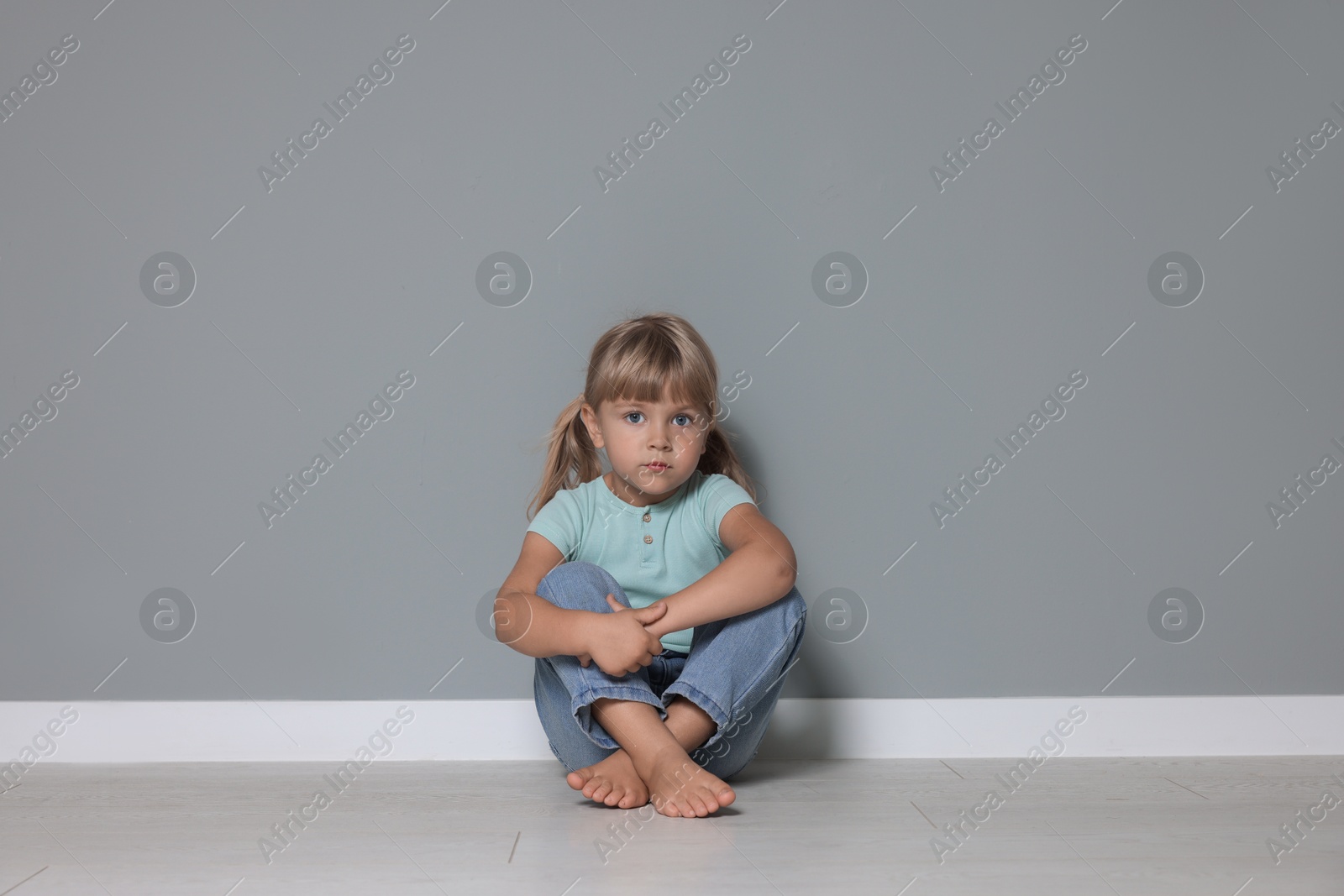 Photo of Orphanage concept. Sad little girl sitting on floor near grey wall