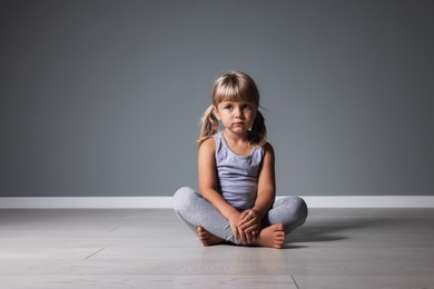 Photo of Orphanage concept. Sad little girl sitting on floor near grey wall